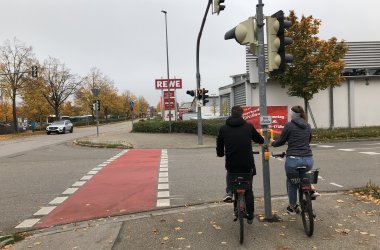 Zwei Radfahrende halten sich am Ampelgriff fest